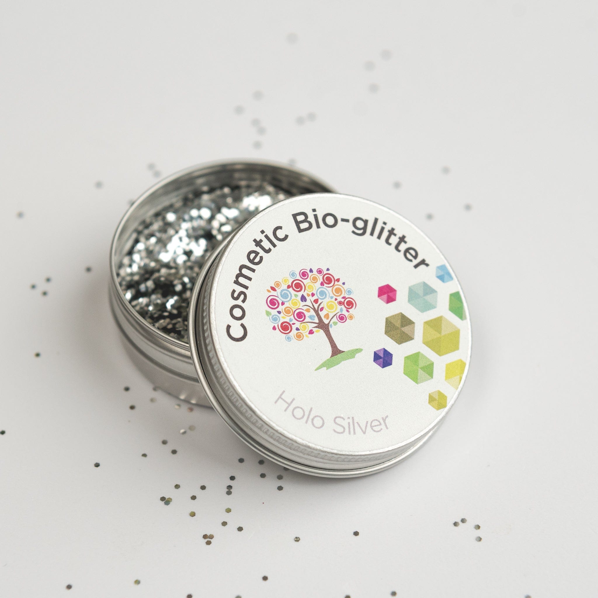 Open pot of The Glitter Tree Holo Silver biodegradable cosmetic glitter with the lid resting on top and glitter sprinkled around the pot
