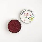 Open pot of The Glitter Tree Red biodegradable cosmetic glitter showing the sparkle texture, next to a closed pot