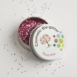 Open tin of The Glitter Tree Rose Pink biodegradable cosmetic glitter with the lid resting on top and glitter sprinkled around the tin