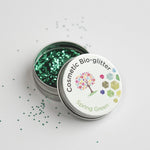Open tin of The Glitter Tree Spring Green biodegradable cosmetic glitter with the lid resting on top and glitter sprinkled around the tin