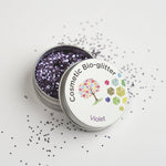 Open tin of The Glitter Tree Violet biodegradable cosmetic glitter with the lid resting on top and glitter sprinkled around the tin